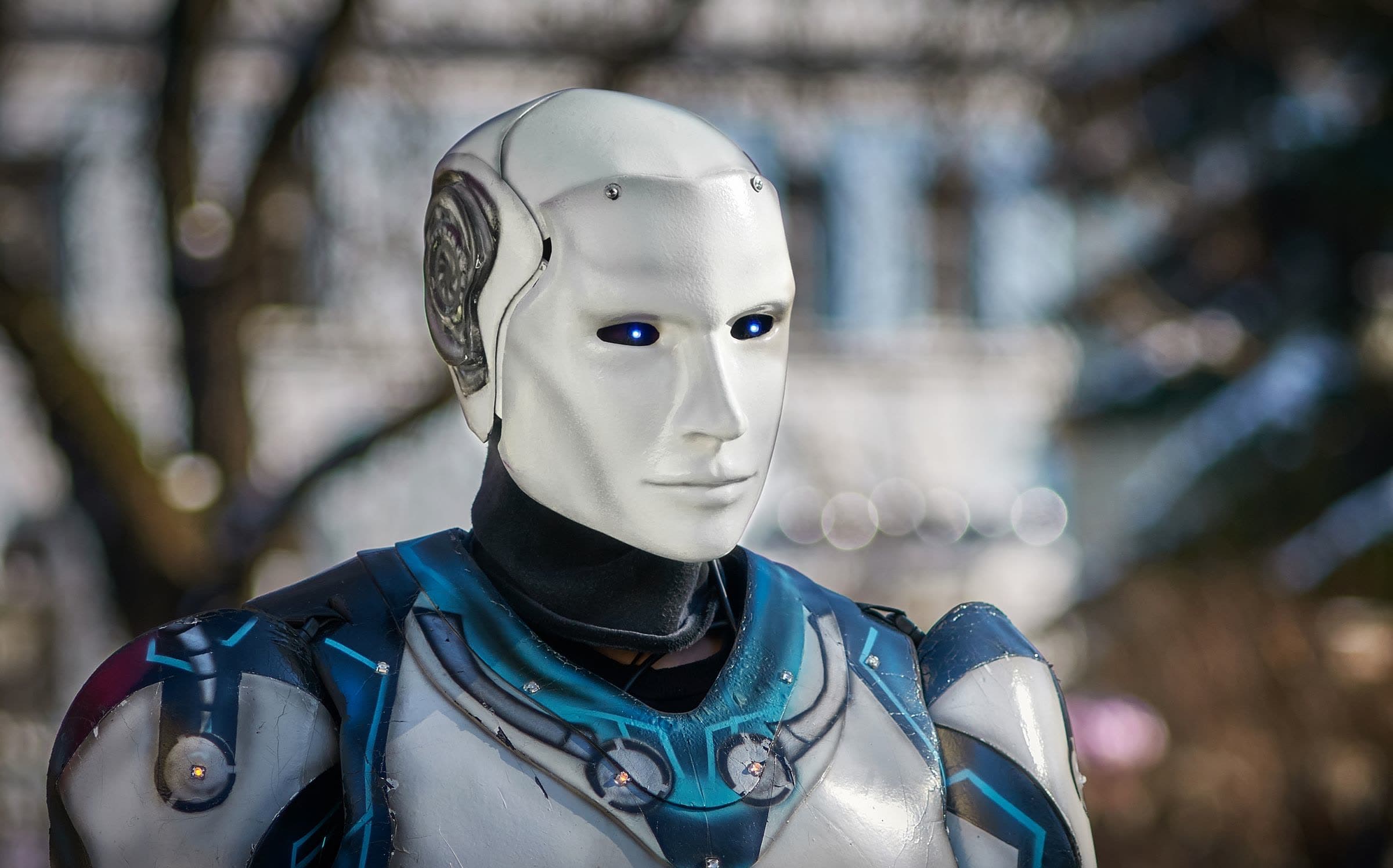 A humanoid robot with a white face and blue-trimmed body outdoors