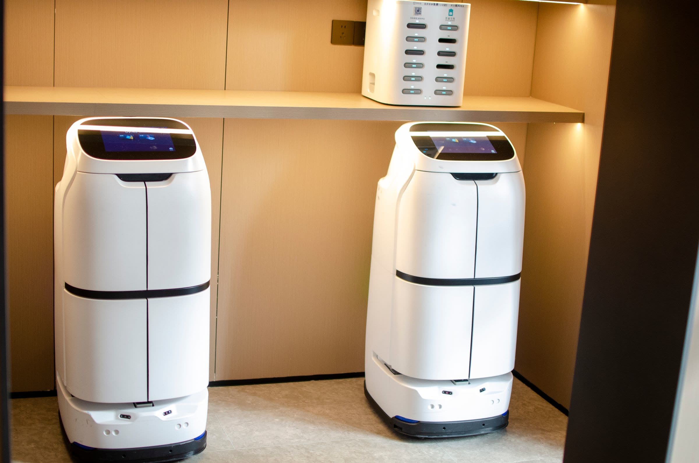 Two white indoor delivery and serving robots parked in a hotel service niche