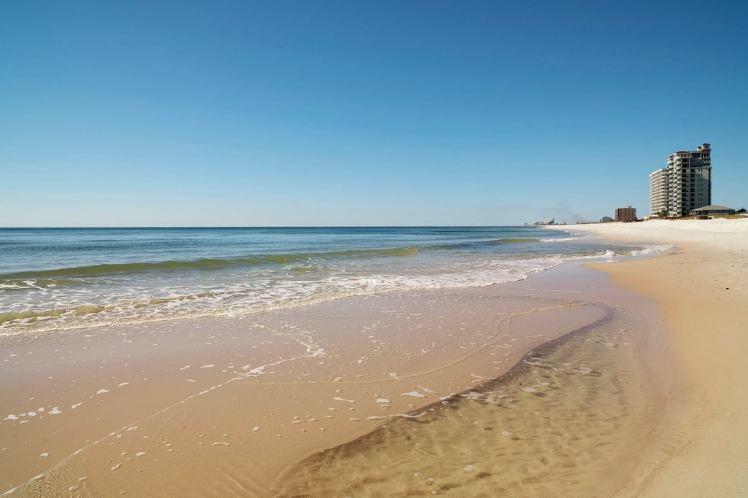 Arena blanca y agua tranquila del Golfo en Perdido Key, con edificios a lo lejos